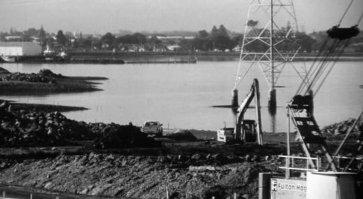 A digger operates near a power tower in the water